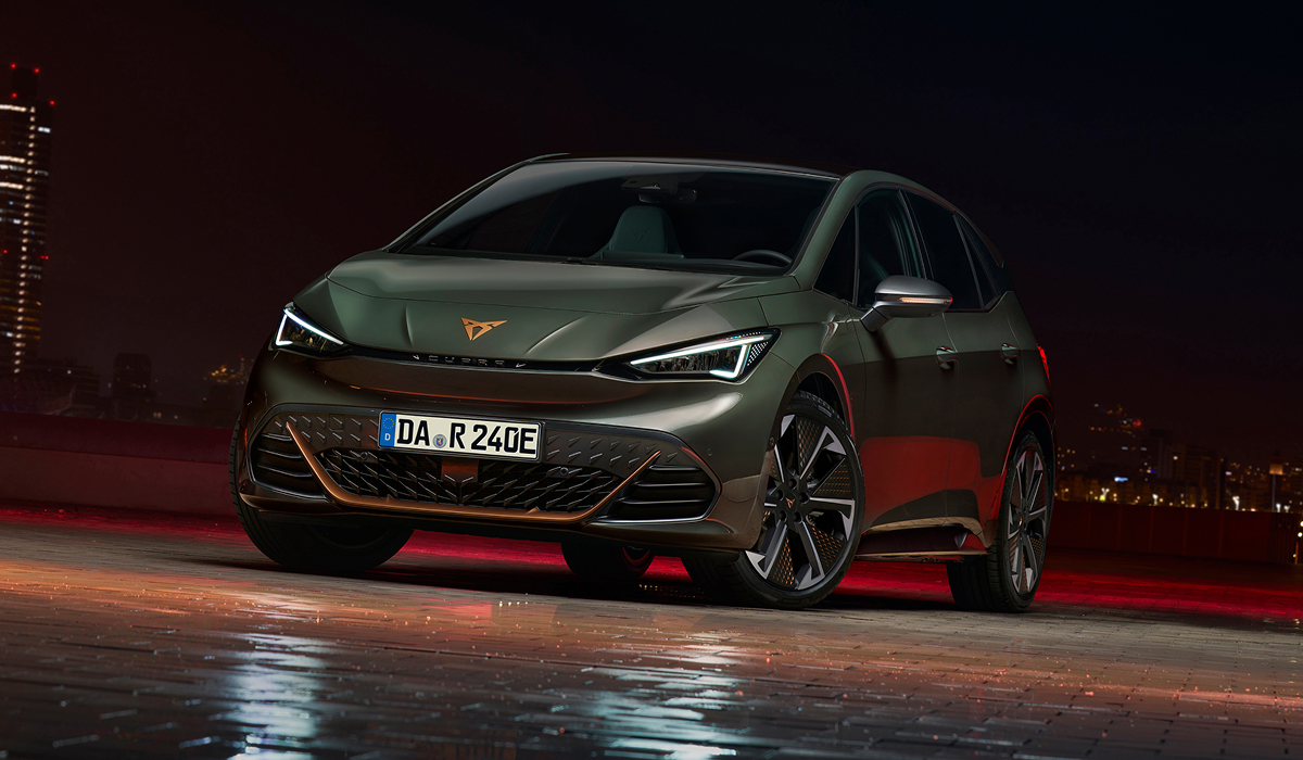 CUPRA Born von vorn rechts auf nasser Fläche bei Nacht mit Stadt im Hintergrund